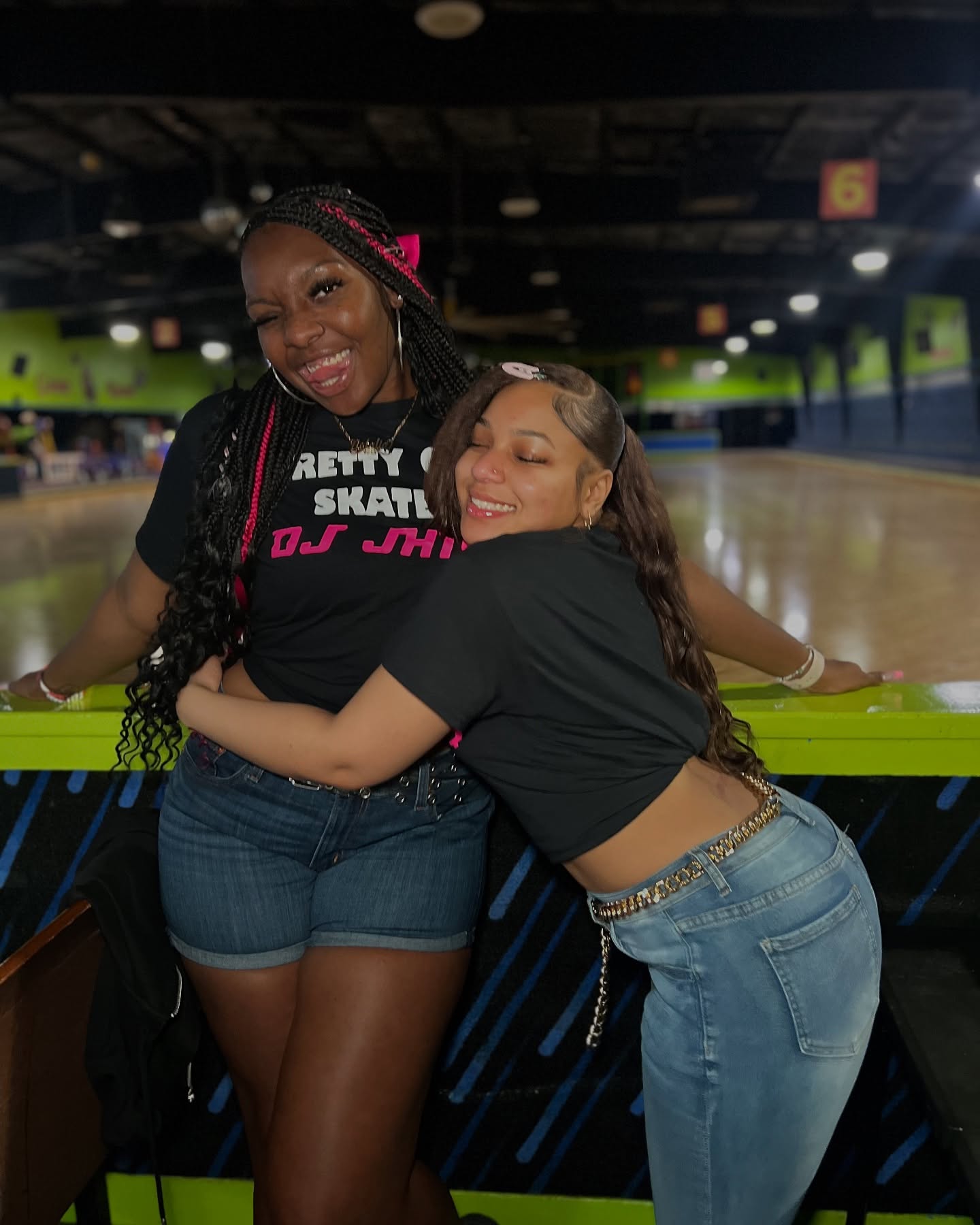 Instagram models @nataliatrue24 on the left and @wingedwheelz on the right wearing black Pretty Girls Skate to DJ J-Hill shirts at the roller rink.