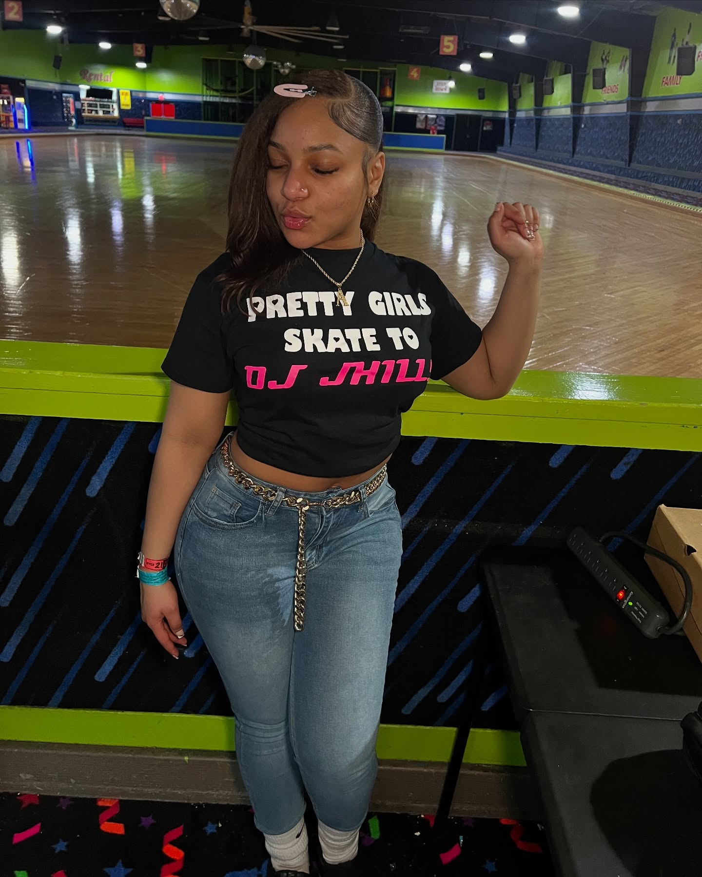 Instagram model @wingedwheelz wearing a black Pretty Girls Skate to DJ J-Hill shirt beside the roller rink floor.